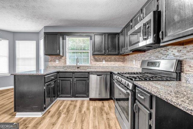 2505 Tiffany Ct, Conyers, GA 30013 - kitchen featuring appliances with stainless steel finishes, a sink, light wood-style floors, a textured ceiling, and light stone countertops