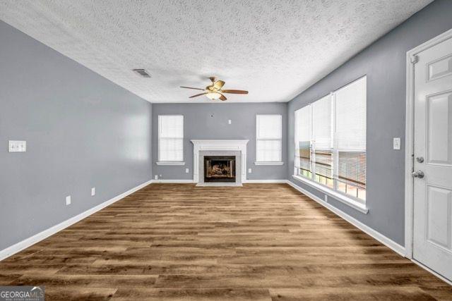 2505 Tiffany Ct, Conyers, GA 30013 - unfurnished living room featuring a ceiling fan, dark wood-style floors, baseboards, a textured ceiling, and a fireplace with flush hearth