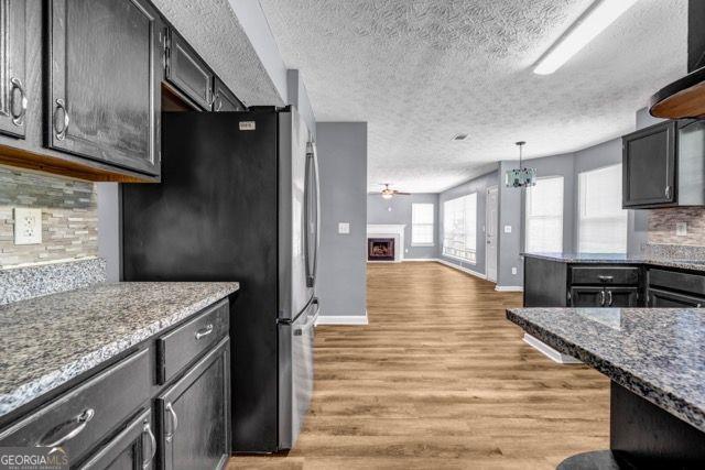 2505 Tiffany Ct, Conyers, GA 30013 - kitchen with freestanding refrigerator, a textured ceiling, tasteful backsplash, light wood-type flooring, and a fireplace