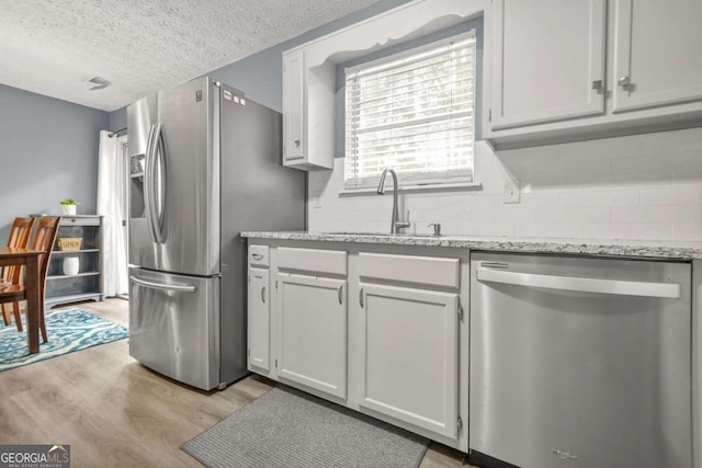 2959 Pritchards Mill Trl, Douglasville, GA 30135 - kitchen with appliances with stainless steel finishes, a sink, light wood-style floors, a textured ceiling, and light stone counters