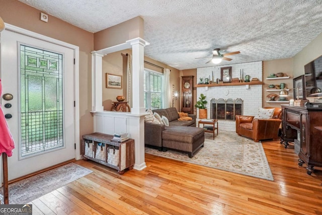 4442 Mclain Cir, Acworth, GA 30101 - living area featuring hardwood / wood-style flooring, a ceiling fan, a brick fireplace, a textured ceiling, and decorative columns