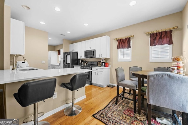 1536 Fenmore St, Lithia Springs, GA 30122 - kitchen featuring appliances with stainless steel finishes, a breakfast bar, light wood-type flooring, white cabinets, and a peninsula