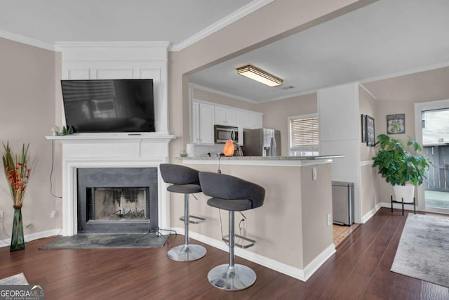 13300 Morris Rd Unit 62, Alpharetta, GA 30004 - kitchen with appliances with stainless steel finishes, white cabinetry, dark wood-type flooring, a fireplace with raised hearth, and a breakfast bar