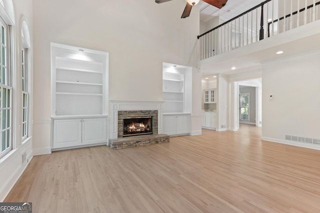140 Longwater Cv, Roswell, GA 30075 - unfurnished living room featuring a towering ceiling, ceiling fan, light wood-style floors, a stone fireplace, and built in shelves