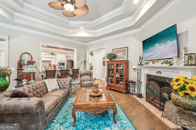 332 Rosshandler Rd, Suwanee, GA 30024 - living room featuring a raised ceiling, light wood-style flooring, a ceiling fan, a fireplace, and ornamental molding