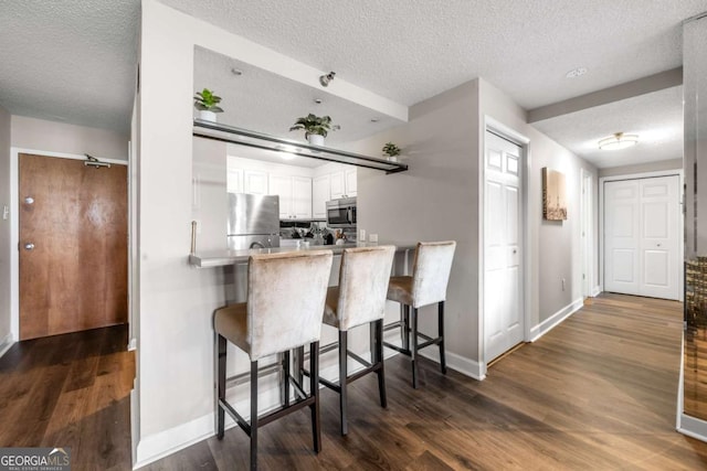 375 Ralph Mcgill Blvd NE Unit 707, Atlanta, GA 30312 - kitchen featuring stainless steel appliances, a textured ceiling, dark wood-type flooring, white cabinets, and a breakfast bar area