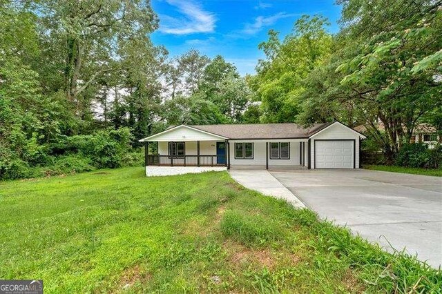 2326 Brackett St SW, Marietta, GA 30060 - ranch-style house with covered porch, a front lawn, a garage, concrete driveway, and view of wooded area