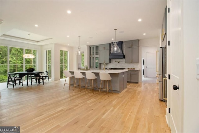 4757 Lake Forrest Dr NW, Atlanta, GA 30342 - kitchen featuring gray cabinetry, premium range hood, a kitchen bar, decorative backsplash, and light countertops