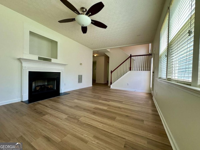 234 Silver Arrow Cir, Austell, GA 30168 - unfurnished living room featuring ceiling fan, stairs, wood finished floors, a textured ceiling, and a fireplace