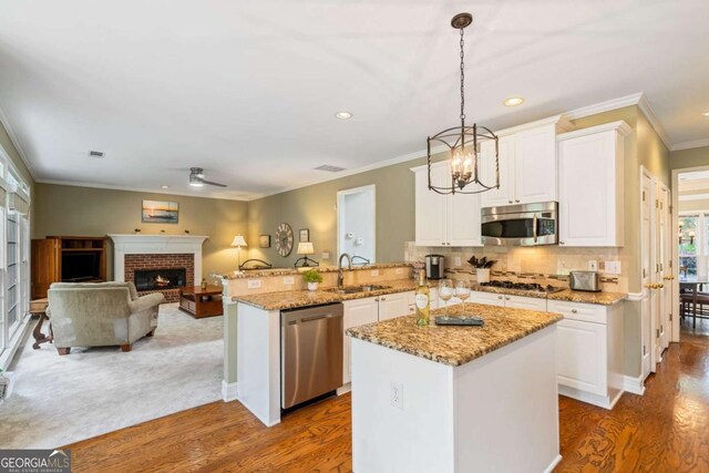 6695 Buckingham Cir, Cumming, GA 30040 - kitchen with appliances with stainless steel finishes, wood finished floors, white cabinetry, a peninsula, and crown molding