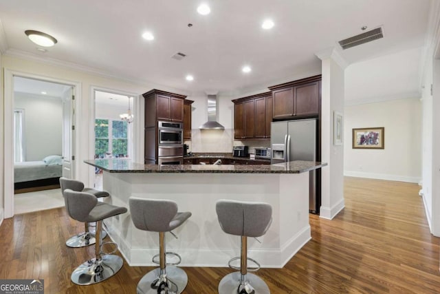 3280 Stillhouse Ln SE Unit 212, Atlanta, GA 30339 - kitchen featuring wall chimney range hood, a breakfast bar area, crown molding, dark brown cabinetry, and dark stone countertops