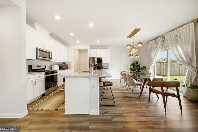 4720 Dufour Dr, Lilburn, GA 30047 - kitchen featuring appliances with stainless steel finishes, a breakfast bar, a kitchen island with sink, white cabinets, and wood finished floors