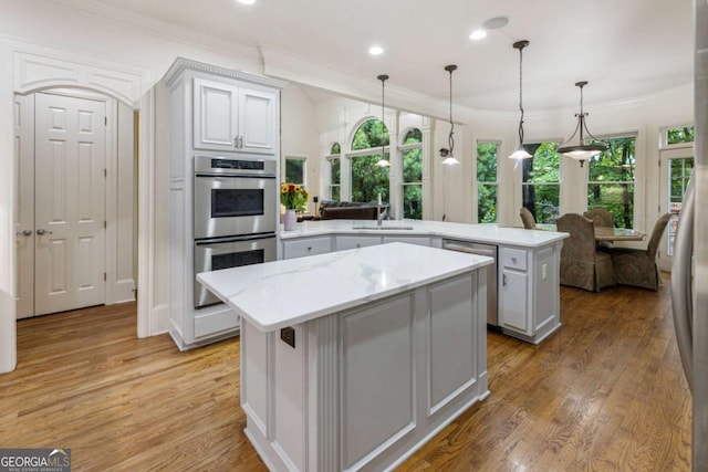 8970 Moor Park Run, Duluth, GA 30097 - kitchen with stainless steel appliances, a peninsula, a kitchen island, light wood-style flooring, and ornamental molding