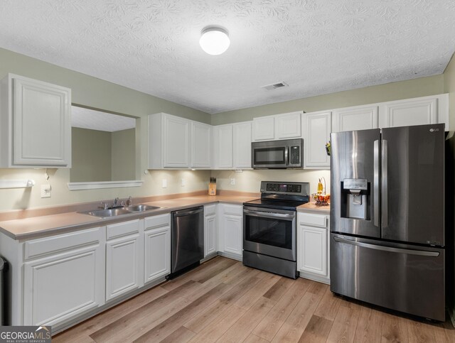 300 Furrow Creek Ct, Jackson, GA 30233 - kitchen with appliances with stainless steel finishes, a sink, light wood-style flooring, white cabinets, and a textured ceiling
