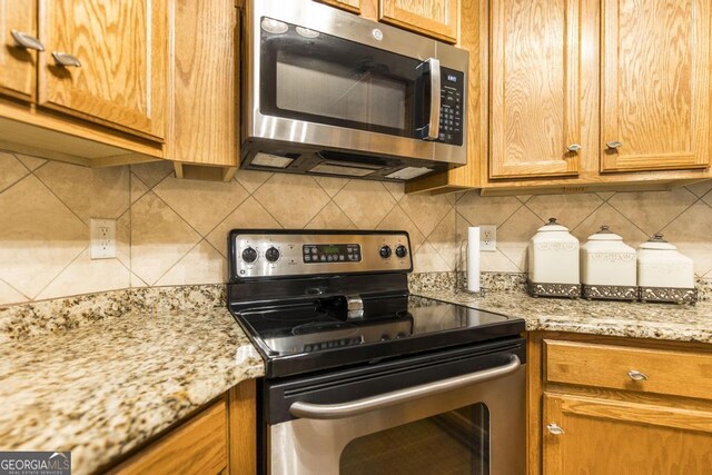 201 Loudon Hill Dr, Warner Robins, GA 31088 - kitchen with appliances with stainless steel finishes, decorative backsplash, light stone countertops, and brown cabinets