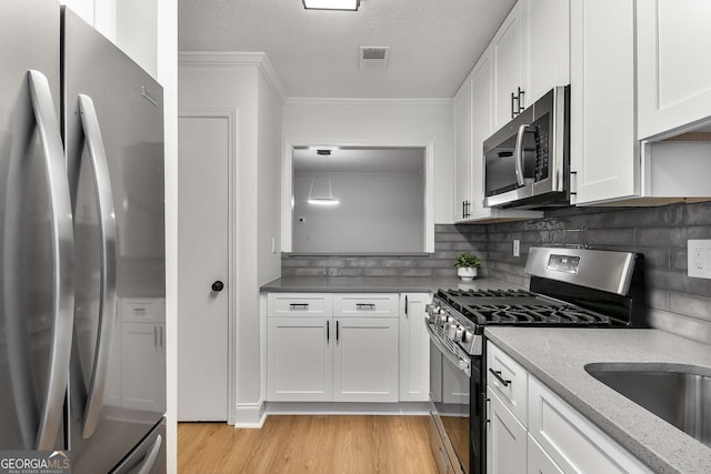 1603 Cumberland Ct, Smyrna, GA 30080 - kitchen featuring appliances with stainless steel finishes, light wood finished floors, white cabinets, crown molding, and tasteful backsplash
