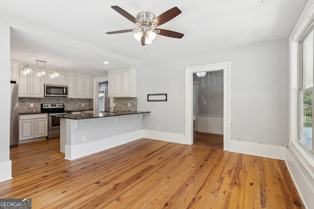 1382 6th Ave, Auburn, GA 30011 - kitchen with appliances with stainless steel finishes, a peninsula, a kitchen breakfast bar, tasteful backsplash, and light wood-type flooring