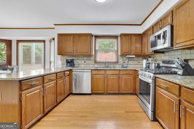 1925 Stonewyck Ct, Cumming, GA 30041 - kitchen featuring appliances with stainless steel finishes, a peninsula, crown molding, light wood-type flooring, and brown cabinets