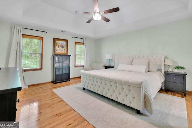1925 Stonewyck Ct, Cumming, GA 30041 - bedroom featuring a tray ceiling, multiple windows, light wood finished floors, and a ceiling fan