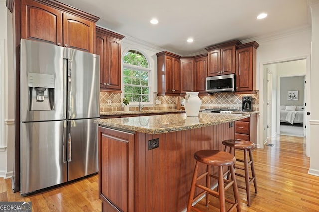 1206 Mountainside Trce NW, Kennesaw, GA 30152 - kitchen with appliances with stainless steel finishes, a kitchen island, ornamental molding, light stone counters, and light wood-style flooring
