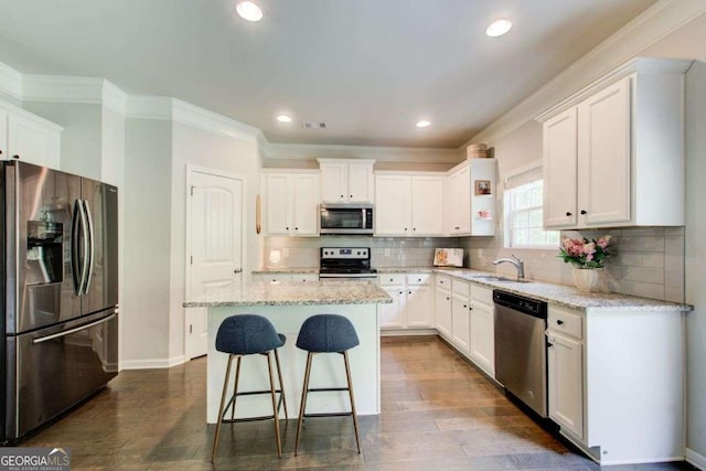 1300 Jefferson Walk Cir, Jefferson, GA 30549 - kitchen featuring appliances with stainless steel finishes, white cabinets, a kitchen bar, a center island, and ornamental molding
