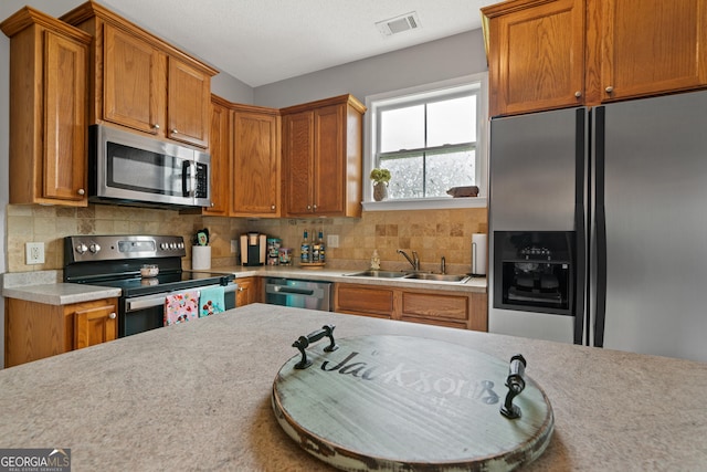 106 Thornton Dr, Bonaire, GA 31005 - kitchen featuring appliances with stainless steel finishes, a sink, light countertops, backsplash, and brown cabinetry