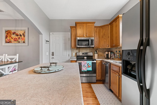 106 Thornton Dr, Bonaire, GA 31005 - kitchen with stainless steel appliances, light countertops, light wood finished floors, backsplash, and brown cabinetry