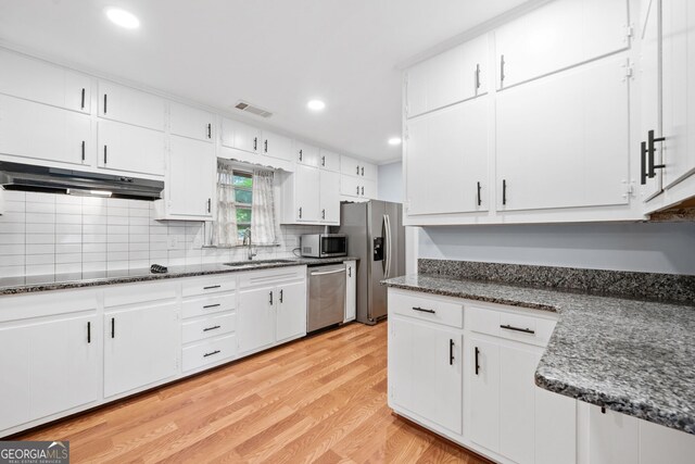 3047 Hudson Ct, Decatur, GA 30033 - kitchen with appliances with stainless steel finishes, under cabinet range hood, light wood finished floors, white cabinetry, and tasteful backsplash