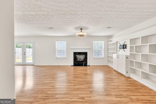 1186 Hawthorn Ln, Grayson, GA 30017 - unfurnished living room featuring light wood-style floors, french doors, a textured ceiling, built in shelves, and a fireplace
