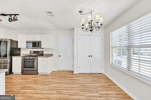 1186 Hawthorn Ln, Grayson, GA 30017 - kitchen with stainless steel appliances, a textured ceiling, a chandelier, white cabinetry, and light wood finished floors