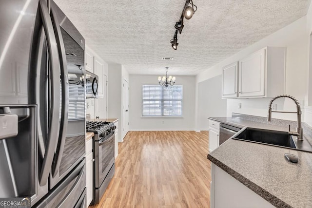 1186 Hawthorn Ln, Grayson, GA 30017 - kitchen featuring stainless steel appliances, a chandelier, light wood finished floors, white cabinetry, and a textured ceiling