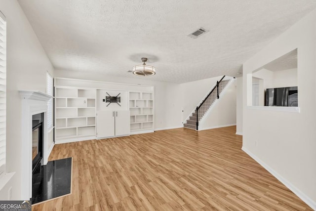 1186 Hawthorn Ln, Grayson, GA 30017 - unfurnished living room featuring a textured ceiling, stairway, light wood-style flooring, and a glass covered fireplace