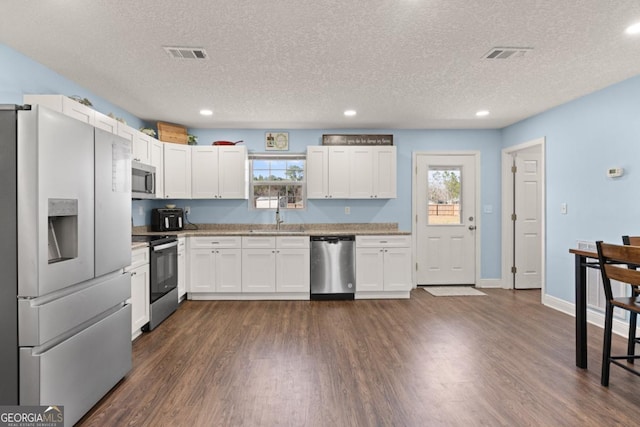 825 Red Hawk Dr, Waynesville, GA 31566 - kitchen featuring appliances with stainless steel finishes, dark wood finished floors, a textured ceiling, healthy amount of natural light, and white cabinets