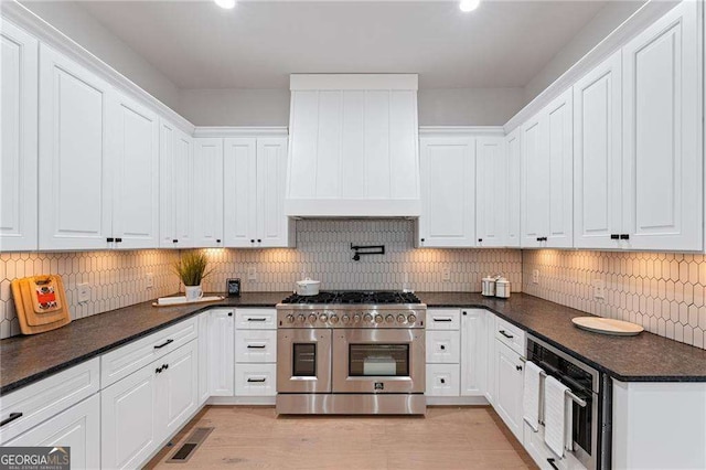 5705 Registry Oaks Ln SE, Mableton, GA 30126 - kitchen featuring stainless steel appliances, custom range hood, dark countertops, white cabinetry, and decorative backsplash