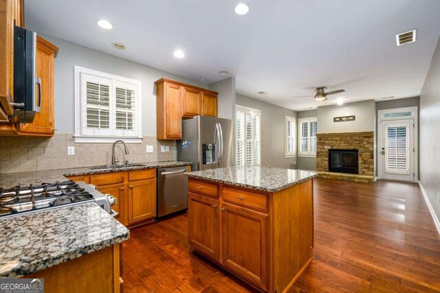 4916 Gathering Pl, Suwanee, GA 30024 - kitchen with appliances with stainless steel finishes, open floor plan, a ceiling fan, light stone countertops, and a fireplace