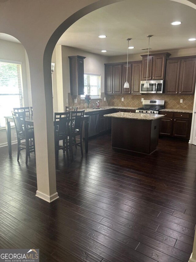 1749 Misselthrush Ln, Mcdonough, GA 30253 - kitchen featuring stainless steel appliances, a kitchen island, arched walkways, decorative backsplash, and dark wood-type flooring