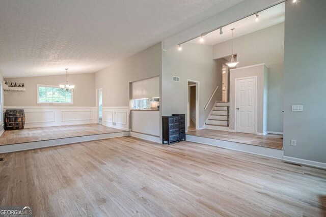 1137 Poplar Log Pl, Austell, GA 30168 - unfurnished living room featuring a chandelier, rail lighting, stairway, wood finished floors, and vaulted ceiling