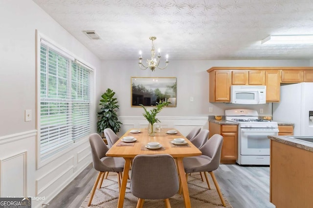 541 Shadow Valley Ct, Lithonia, GA 30058 - dining room with light wood-type flooring, a chandelier, a wainscoted wall, and a textured ceiling
