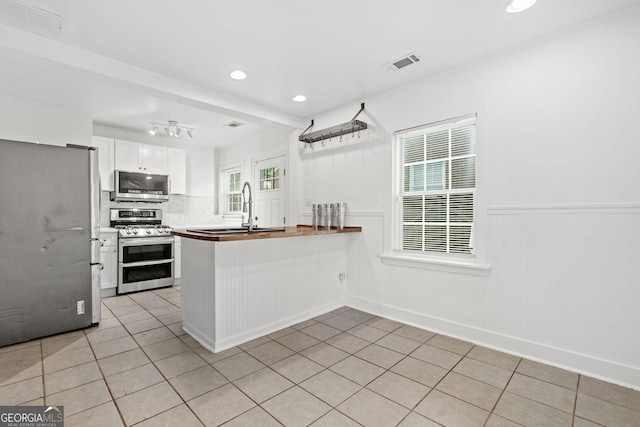 1844 Stanton St, Decatur, GA 30032 - kitchen featuring appliances with stainless steel finishes, a peninsula, white cabinets, light tile patterned flooring, and a sink