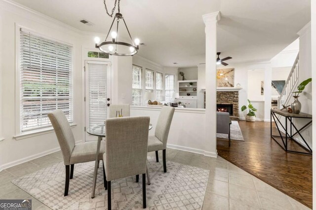 5860 Fairway View Dr, Suwanee, GA 30024 - dining area with ornamental molding, a chandelier, tile patterned flooring, a ceiling fan, and a stone fireplace