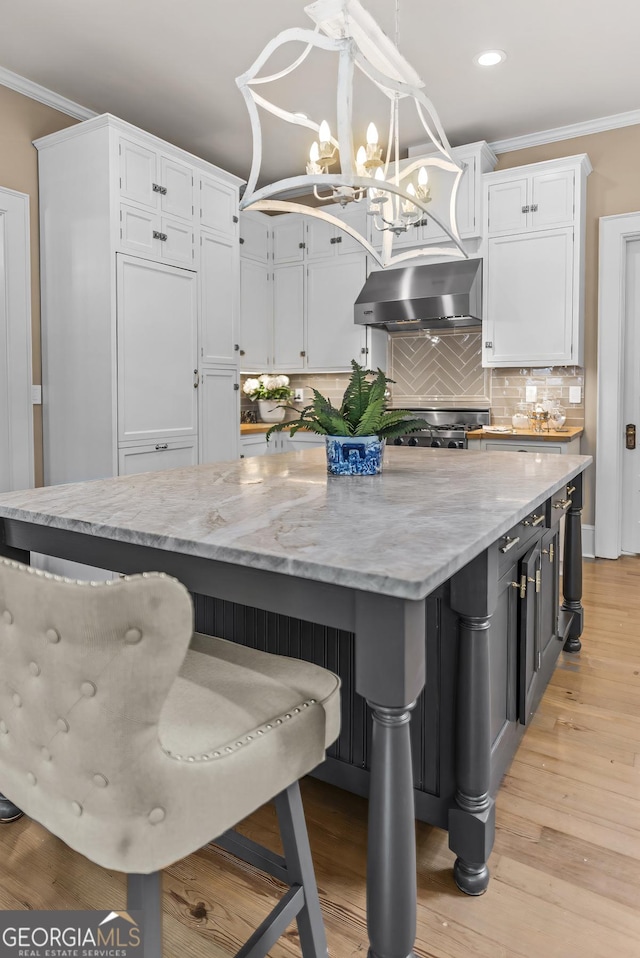 766 E Ave, Madison, GA 30650 - kitchen featuring wall chimney exhaust hood, white cabinetry, crown molding, a chandelier, and light stone counters