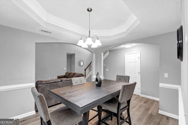 3190 Water Brook Dr SW, Conyers, GA 30094 - dining room with arched walkways, a tray ceiling, a chandelier, light wood finished floors, and stairway