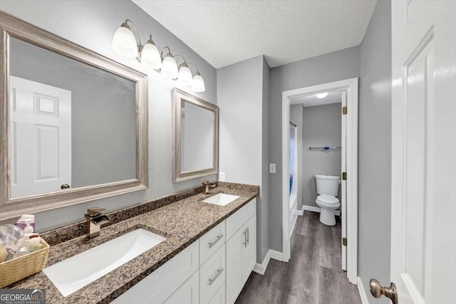 3190 Water Brook Dr SW, Conyers, GA 30094 - bathroom with double vanity, wood finished floors, toilet, baseboards, and a textured ceiling