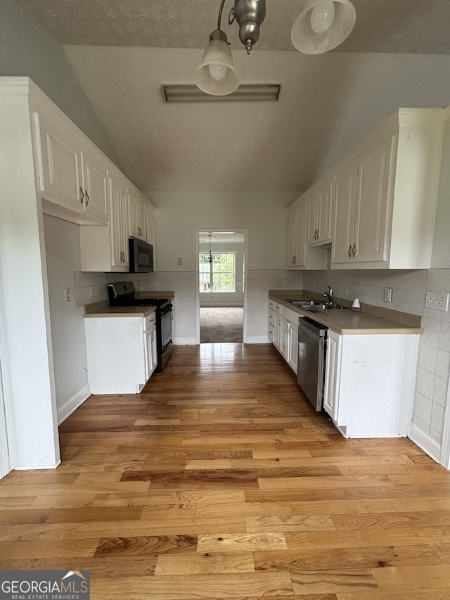 4069 Savannah Ridge Ct, Loganville, GA 30052 - kitchen with gas range oven, stainless steel dishwasher, lofted ceiling, white cabinetry, and light wood finished floors