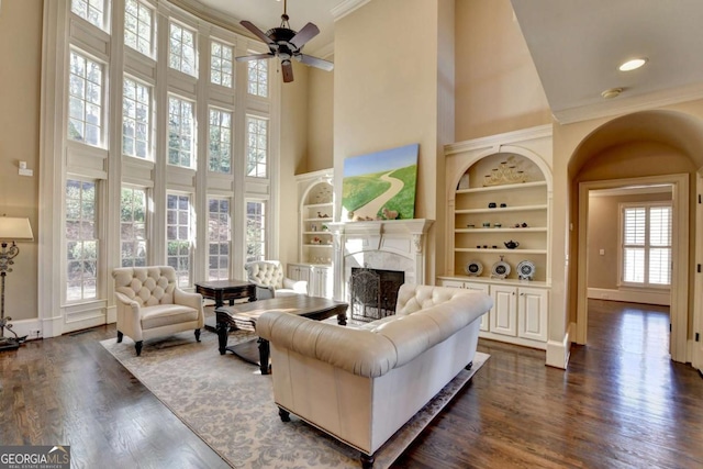 10125 Brixton Pl, Suwanee, GA 30024 - living area featuring a towering ceiling, built in shelves, a premium fireplace, crown molding, and dark wood-style flooring