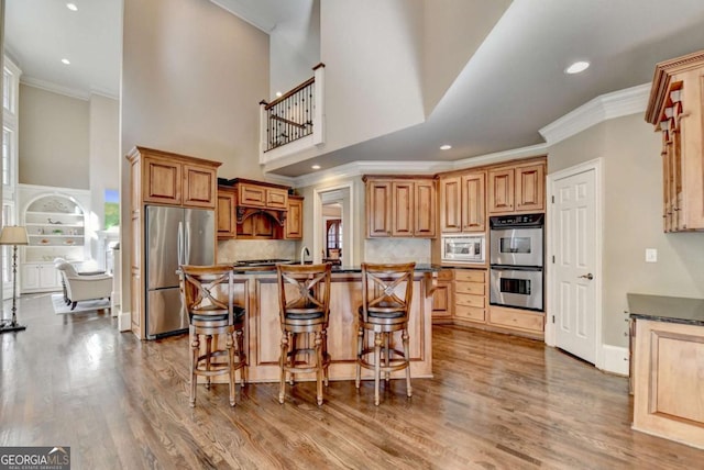 10125 Brixton Pl, Suwanee, GA 30024 - kitchen with appliances with stainless steel finishes, crown molding, dark countertops, a breakfast bar area, and a high ceiling