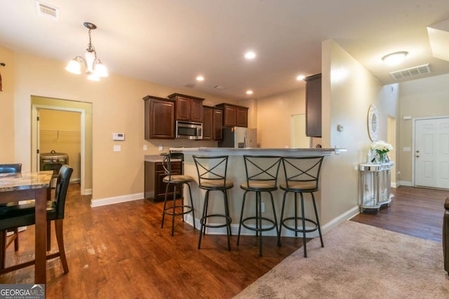 12275 Styron Dr, Hampton, GA 30228 - kitchen with appliances with stainless steel finishes, a chandelier, a kitchen breakfast bar, dark wood finished floors, and a peninsula