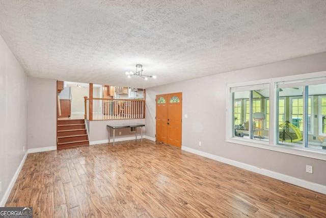2201 Colonial Oak Way, Stone Mountain, GA 30087 - unfurnished living room with wood finished floors, a chandelier, stairway, a textured ceiling, and baseboards