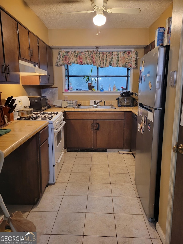 106 Garden Trl, Stockbridge, GA 30281 - kitchen with under cabinet range hood, freestanding refrigerator, gas range gas stove, light countertops, and a textured ceiling