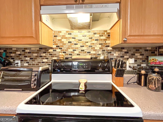 6830 Peeksville Rd, Mcdonough, GA 30252 - kitchen with range with electric cooktop, under cabinet range hood, light brown cabinets, tasteful backsplash, and light countertops